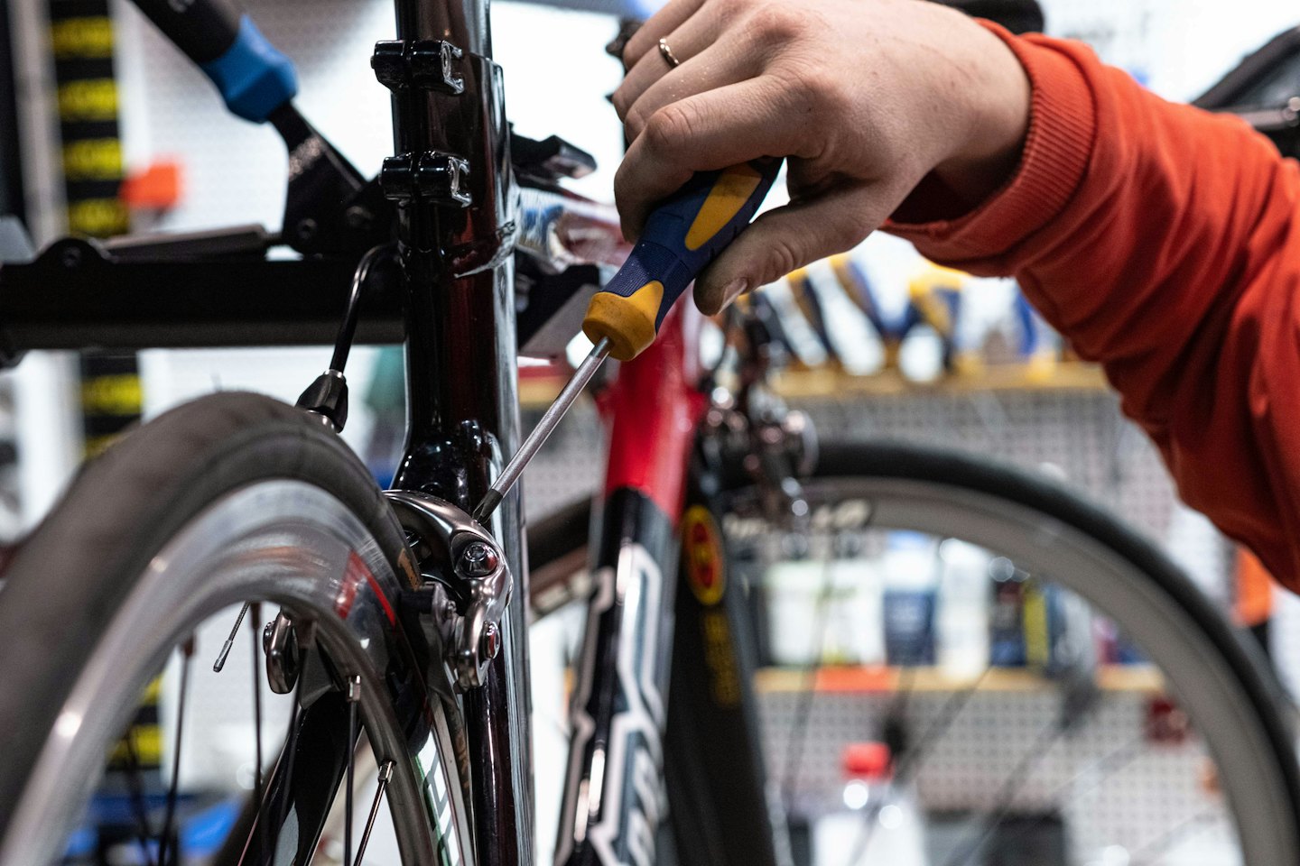 Hand med orange ärm reparerar cykelbromsar med skruvmejsel.